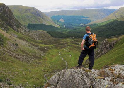 A walker standing on a rock enjoying the view over Corrie Fee in Glen Clova, Scotland