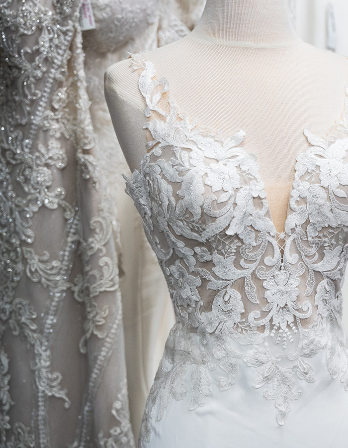 A brides dress on a mannequin next to lots of brides dresses on a rail in a bridal. wear shop.