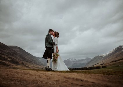 A bride and groom embracing in Glen Clova with snow capped mountains by them. Photography by Burfly. https://burfly.co.uk/