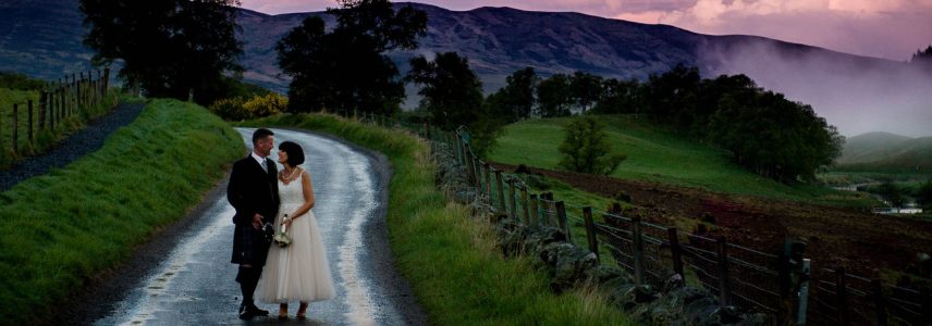 A bride and groom at sunset in Glen Clova on a winding country road. Photography by FMV Photography. https://www.fmvphotography.co.uk/