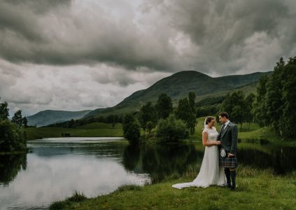 A bride and groom standing by a Scottish Loch in Glen Clova on a moody Scottish day. Photography by Burfly. https://burfly.co.uk/