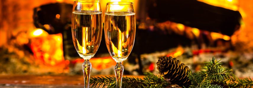 Two glasses of champagne buy fire next to Christmas decorations