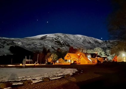 Glen Clova Hotel at night with snowcapped mountains and a starry night behind the hotel lit up in the darkness
