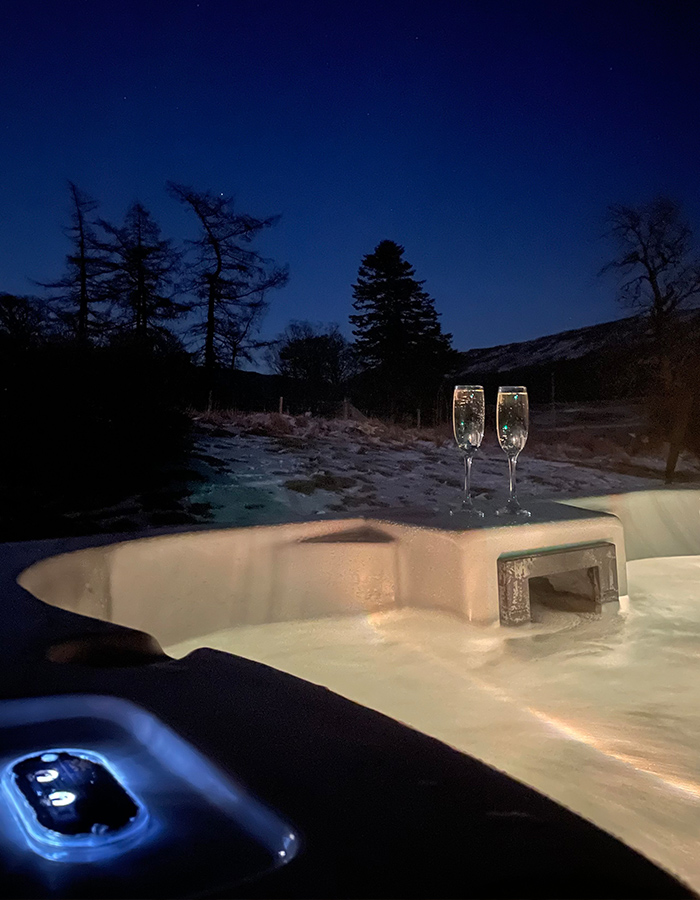 A hot tub with two champagne glasses on it on a snowy winters night in a Clova Lodge at Glen Clova Hotel and Lodges