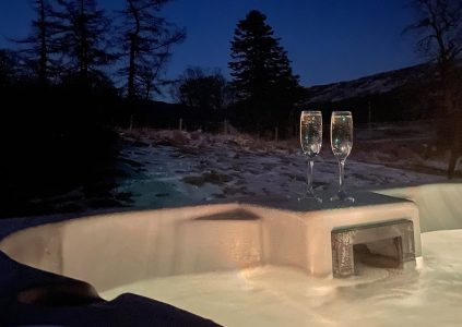 A hot tub with two champagne glasses on it on a snowy winters night in a Clova Lodge at Glen Clova Hotel and Lodges